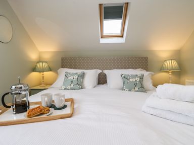 A bedroom with a double bed two pillows with floral covers bedside lamps a skylight window and a tray with coffee and pastries on the bed at Rose Cottage Faceby near Swainby