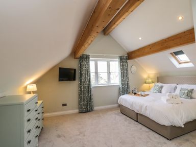A bedroom with a large bed bedside lamps a chest of drawers and wooden ceiling beams at Rose Cottage Faceby near Swainby