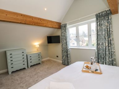 A bedroom with two dressers a wall-mounted tv a window with floral curtains and a bed with a tray of coffee and pastries at Rose Cottage in Faceby near Swainby