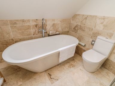 A bathroom with a white bathtub a towel hanging on the tub a toilet and beige tiled walls and floor at Rose Cottage Faceby near Swainby