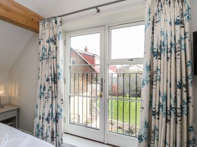 A bedroom window with blue and white curtains overlooking a garden at Rose Cottage in Faceby near Swainby