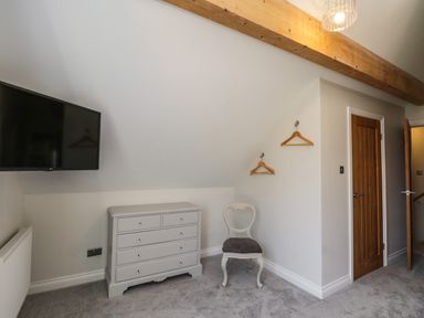 A bedroom corner with a wall-mounted television a chest of drawers a chair and wooden door at Rose Cottage Faceby near Swainby