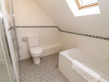 A bathroom with a toilet bathtub with towel tiled floor and slanted ceiling skylight at Rose Cottage Faceby near Swainby