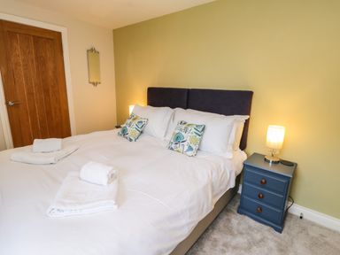 A bedroom with a bed with white linens and patterned pillows next to a blue bedside table with a lamp at Rose Cottage in Faceby near Swainby