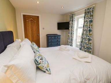 A bedroom with a bed with white bedding and floral pillows a wooden door a blue chest of drawers and window with floral curtains at Rose Cottage Faceby near Swainby