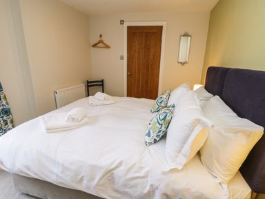 A bedroom with a bed with white linens and patterned pillows a wooden door and a chair at Rose Cottage in Faceby near Swainby