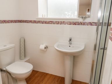 A bathroom with a toilet sink shower and tiled walls with a colored border at Rose Cottage in Faceby near Swainby