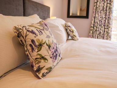 A bed with white linens and floral pillows in a bedroom with a mirror and floral curtains at Rose Cottage Faceby near Swainby