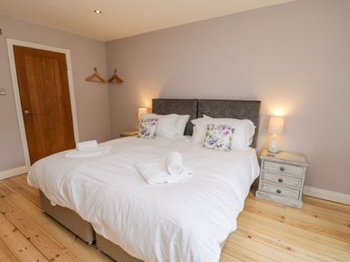 A bedroom with a double bed with white linens two bedside tables with lamps a wooden door and two wall hooks with hangers at Rose Cottage Faceby near Swainby