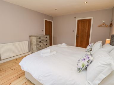A bedroom with a bed and floral pillows a chest of drawers and wooden doors at Rose Cottage Faceby near Swainby