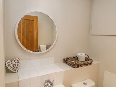 A bathroom with a round mirror above a tiled ledge with a wicker basket holding toilet paper at Rose Cottage Faceby near Swainby