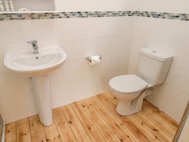 A bathroom with a pedestal sink toilet wooden floor and tiled walls at Rose Cottage Faceby near Swainby