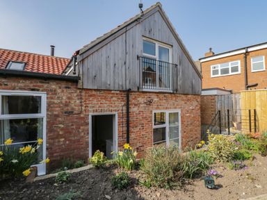 A brick house with a wooden upper floor and a garden with flowers at Rose Cottage in Faceby near Swainby