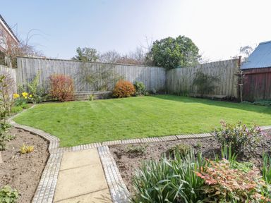 A backyard with a grass lawn surrounded by plants and wooden fences at Rose Cottage Faceby near Swainby