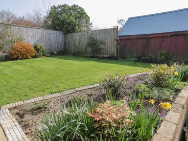 A garden with a green lawn flower beds and a wooden fence at Rose Cottage Faceby near Swainby