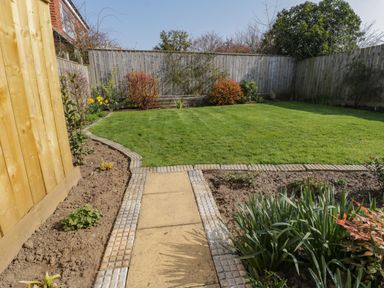 A garden with a grass lawn bordered by a stone and concrete pathway and a wooden fence at Rose Cottage in Faceby near Swainby