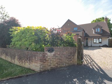 A detached house with a tiled roof and gravel driveway behind a brick wall with green bushes at Morgan House in Middlezoy