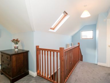 A hallway with a wooden staircase railing a chest of drawers with a vase on top and two windows at Morgan House in Middlezoy
