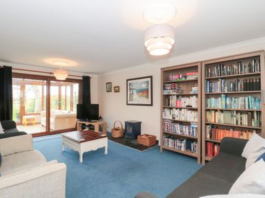 A living room with bookshelves a coffee table sofas and a television near large glass doors leading to a sunroom at Morgan House in Middlezoy