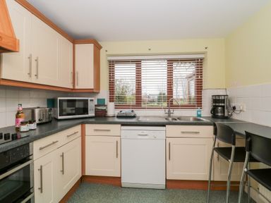 A kitchen with cream cabinets a microwave a dishwasher a double sink a coffee maker and two black chairs by a counter at Morgan House in Middlezoy