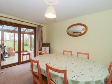 A dining room with a wooden table covered by a patterned tablecloth and wooden chairs near glass sliding doors at Morgan House in Middlezoy