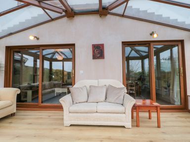 A sitting area with a beige sofa and a wooden side table in front of sliding glass doors at Morgan House in Middlezoy