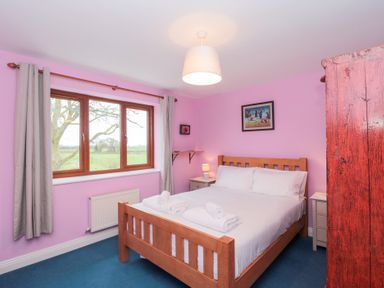 A bedroom with a double bed and rolled towels on it beside two nightstands and a window with curtains at Morgan House in Middlezoy