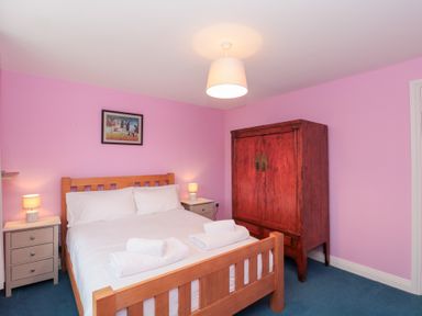 A bedroom with a wooden bed and white bedding with towels on it two bedside tables with lamps and a red wooden wardrobe at Morgan House in Middlezoy
