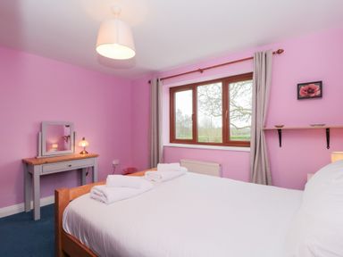 A bedroom with a wooden bed with white bedding and towels a dressing table with a mirror a window with curtains and a wall shelf with a small framed picture at Morgan House in Middlezoy