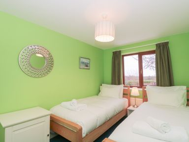 A bedroom with two single beds with white linens a white cabinet a round mirror on the wall and a window with green curtains at Morgan House in Middlezoy