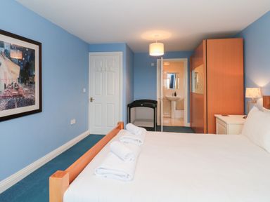 A bedroom with a bed with white sheets and towels on it a wardrobe a nightstand with a lamp and an open door showing a bathroom at Morgan House in Middlezoy
