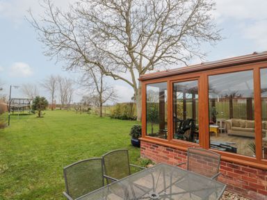 A garden with metal patio table and chairs next to a conservatory with furniture and exercise equipment at Morgan House in Middlezoy