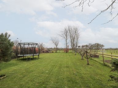 A garden with a trampoline several leafless trees and a wooden fence at Morgan House in Middlezoy
