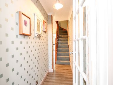 A hallway with patterned wallpaper a carpeted staircase and framed pictures at 57 Southend Road Hunstanton