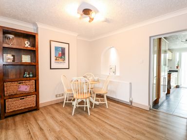 A dining area with a wooden table and four chairs next to an open doorway leading to a kitchen at 57 Southend Road Hunstanton