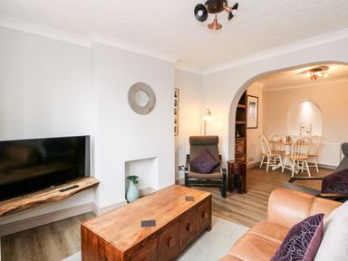 A living room with a wooden coffee table television on a wall shelf and an archway leading to a dining area at 57 Southend Road in Hunstanton