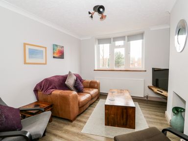 A living room with a brown leather sofa a wooden coffee table and a wall-mounted television at 57 Southend Road in Hunstanton