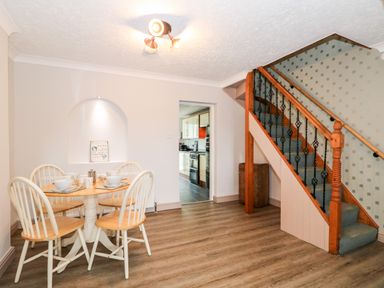 A dining area with a round wooden table and four chairs next to a staircase and an open doorway to a kitchen at 57 Southend Road Hunstanton