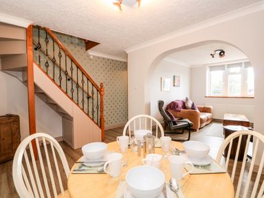 A dining area with set table and chairs next to a staircase and a living room with sofa and armchair at 57 Southend Road Hunstanton