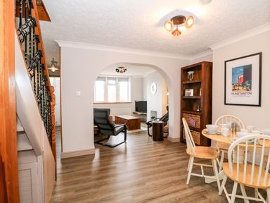A dining area with a round wooden table and chairs next to an open archway leading to a living room with chairs and a coffee table at 57 Southend Road Hunstanton