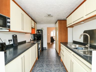 A galley kitchen with cream cabinets a black countertop a double sink a microwave a toaster and a black refrigerator at 57 Southend Road in Hunstanton