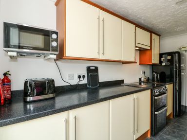 A kitchen with black countertop cabinets a microwave toaster fire extinguisher oven and a refrigerator at 57 Southend Road Hunstanton