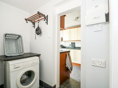 A utility room with a washing machine laundry basket and a wall rack leading into a kitchen at 57 Southend Road in Hunstanton
