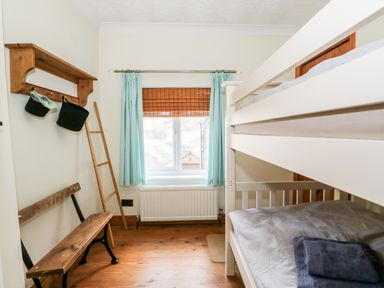 A small bedroom with a bunk bed a wooden bench and a window with blue curtains at 57 Southend Road Hunstanton