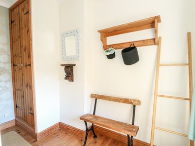 A corner room with a wooden bench a wooden ladder a wall shelf with hooks and two hanging baskets a small wall mirror and a wooden closet at 57 Southend Road Hunstanton