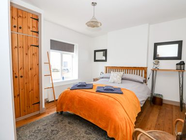 A bedroom with a wooden bed, orange blanket, two mirrors, wooden floor and a wooden wardrobe at 57 Southend Road in Hunstanton