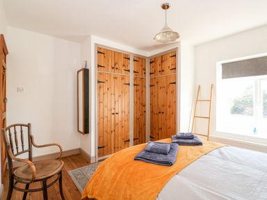 A bedroom with wooden corner wardrobes a chair a bed with folded towels on an orange blanket and a window with a gray blind at 57 Southend Road Hunstanton
