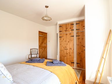 A bedroom with a bed, wooden wardrobe, wooden door, chair, and a wooden ladder at 57 Southend Road in Hunstanton