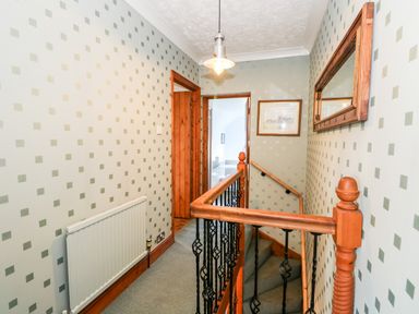 A hallway with patterned wallpaper radiator a hanging light fixture a wooden banister with black metal spindles and doors leading to other rooms at 57 Southend Road Hunstanton
