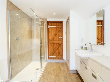 A bathroom with a glass shower enclosure a wooden door a sink with a mirror and cabinets at 57 Southend Road in Hunstanton